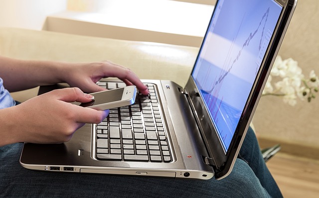 Person on couch with laptop and cell phone, studying Spanish online.